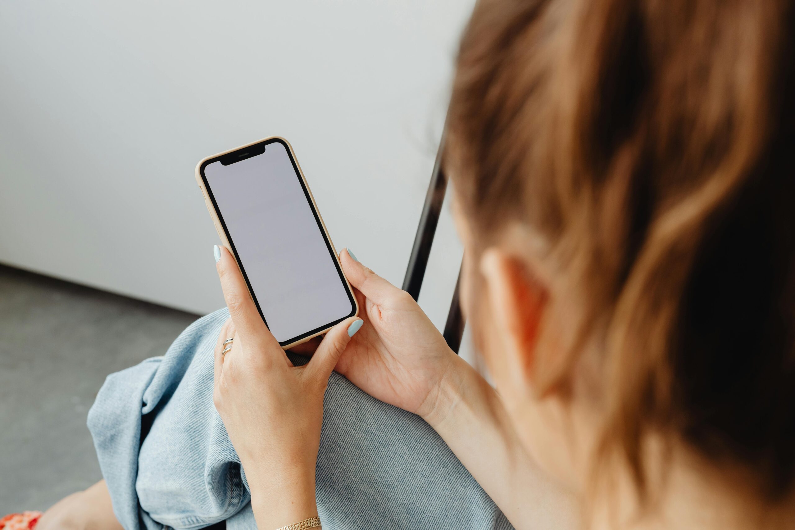 A woman holds a smartphone with a blank screen indoors, offering a mockup opportunity.